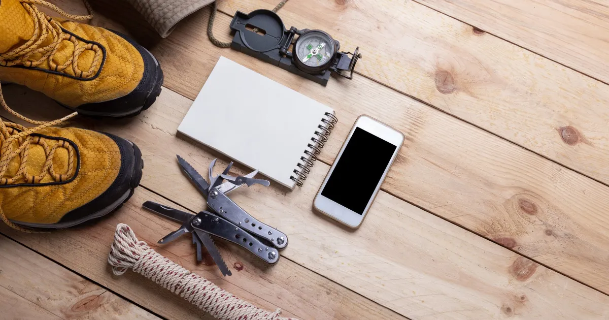 Equipo de supervivencia y material de camping organizado sobre superficie plana, incluyendo mochila, herramientas y suministros para bolsa de 72 horas