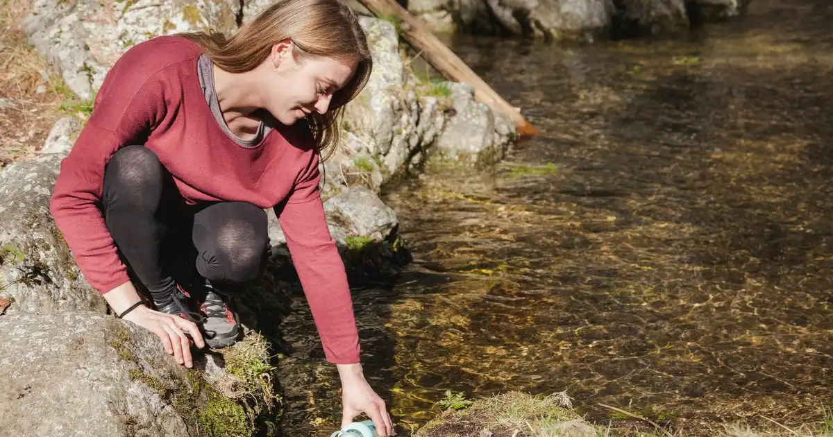 Persona llenando una cantimplora en un río de montaña, comparativa de métodos de potabilización de agua para emergencias