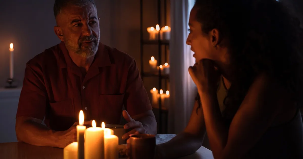 Casal em casa durante um apagão, à luz de velas, preparando-se para a emergência