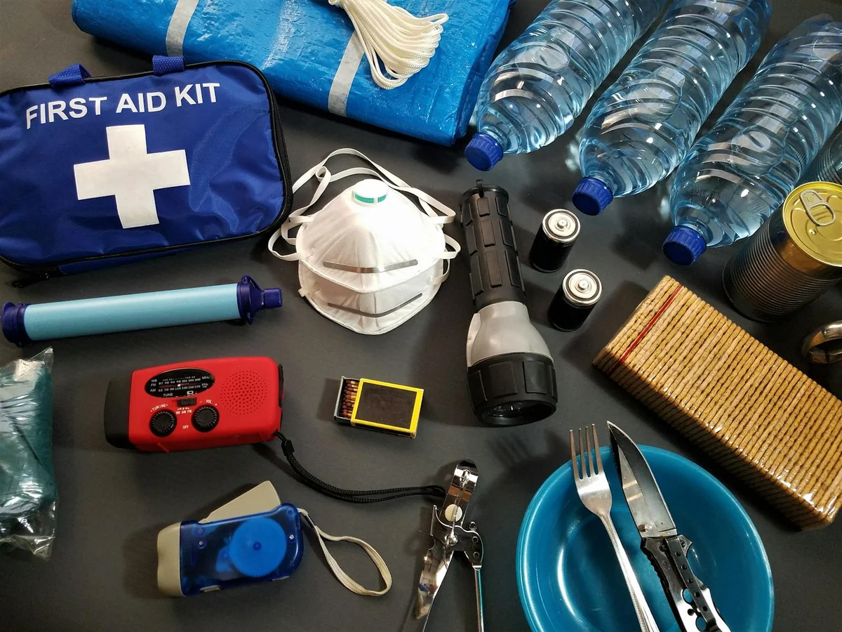 Kit de emergência 72 horas exposto sobre uma mesa de madeira com água, comida, lanterna e primeiros socorros
